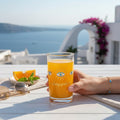 Mati Made Always Protected small glass with blue eye motif filled with orange juice on a sunny Mediterranean terrace.