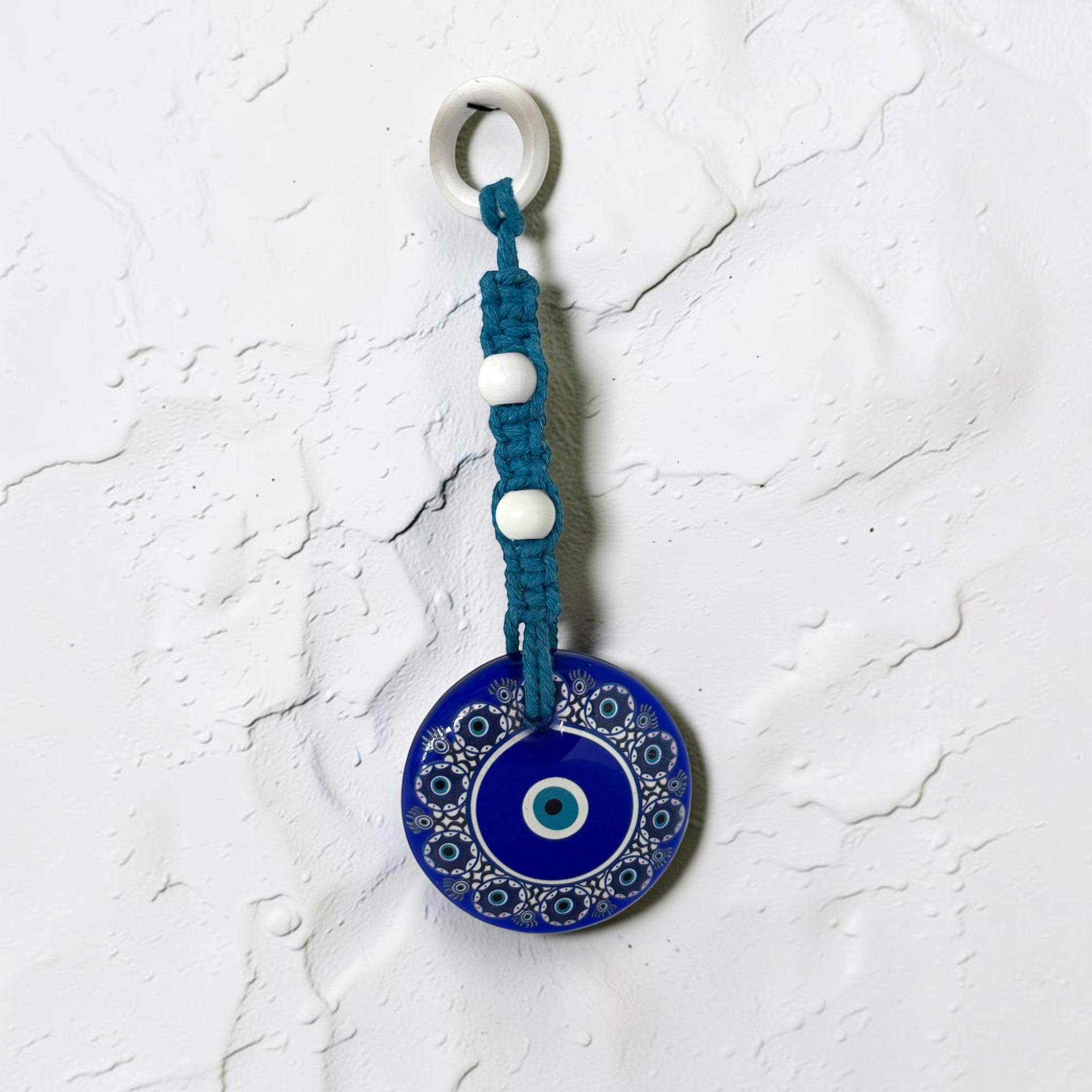 Mati Made Azure Disc wall charm featuring a blue acrylic evil eye pendant with braided cord and white accent beads.