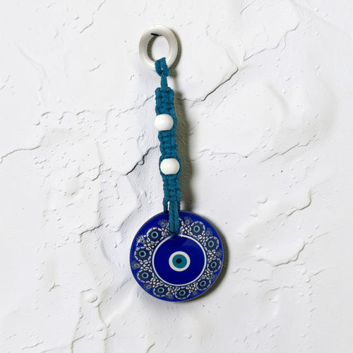 Mati Made Azure Disc wall charm featuring a blue acrylic evil eye pendant with braided cord and white accent beads.