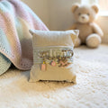 Mati Made decorative baby keepsake pin with gold ribbon, evil eye, baby bottle, and rocking horse charms on a pillow.