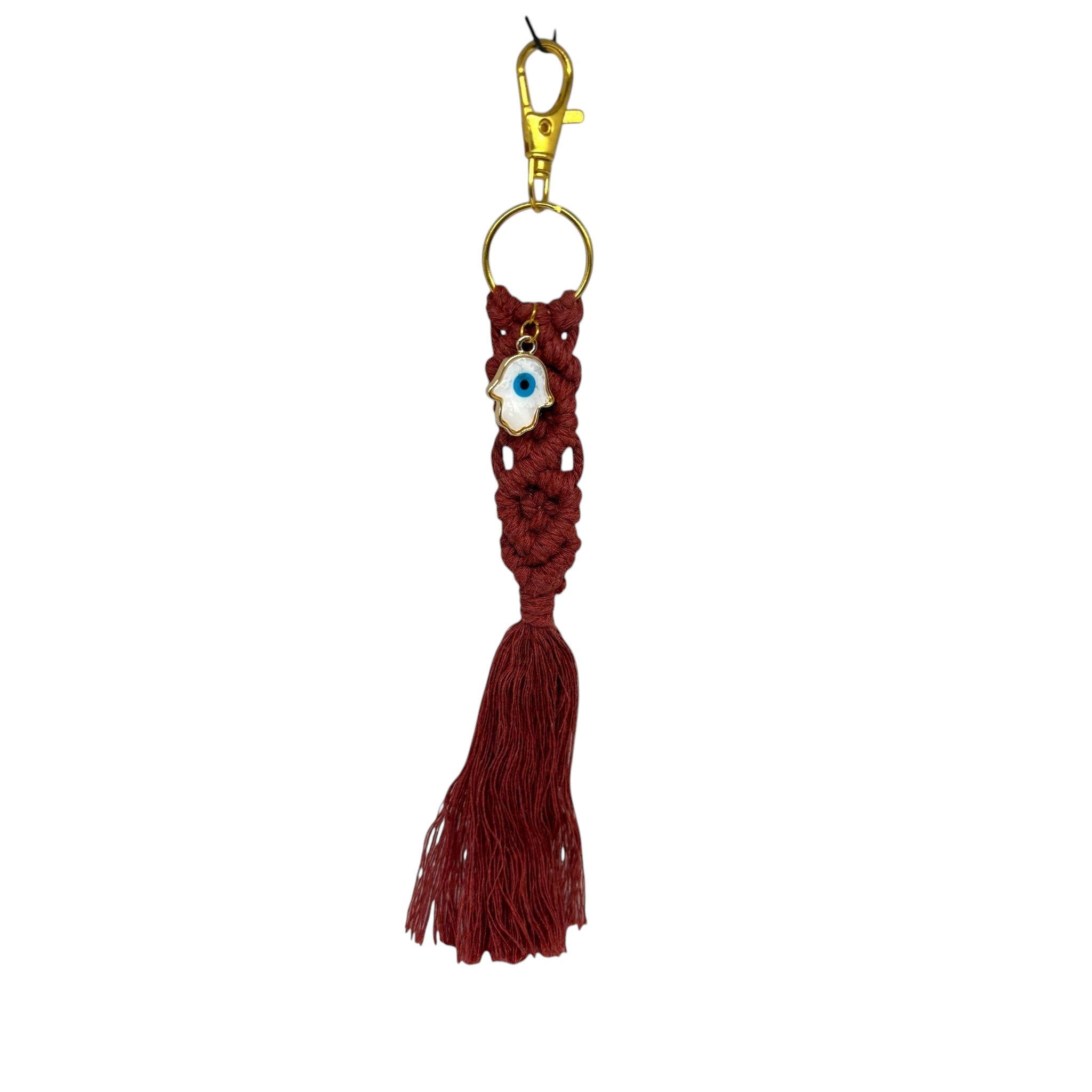 Mati Made burgundy macrame keychain with a white Hamsa charm and gold clasp hardware against a white textured wall.