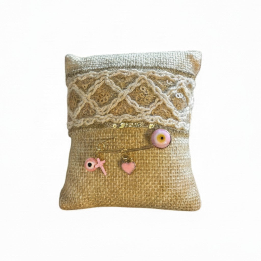 Mati Made handcrafted burlap filaxto pillow with lace trim and a gold brooch featuring a pink mati, heart, and cross.