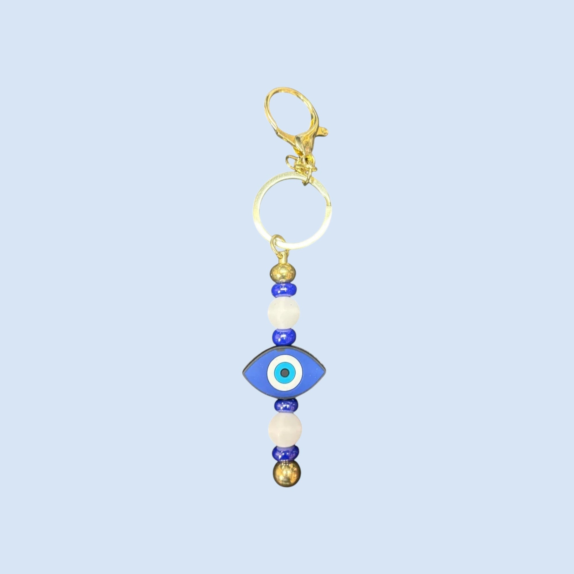 Mati Made decorative evil eye bag charm with blue glass, white beads, and polished gold-tone hardware.