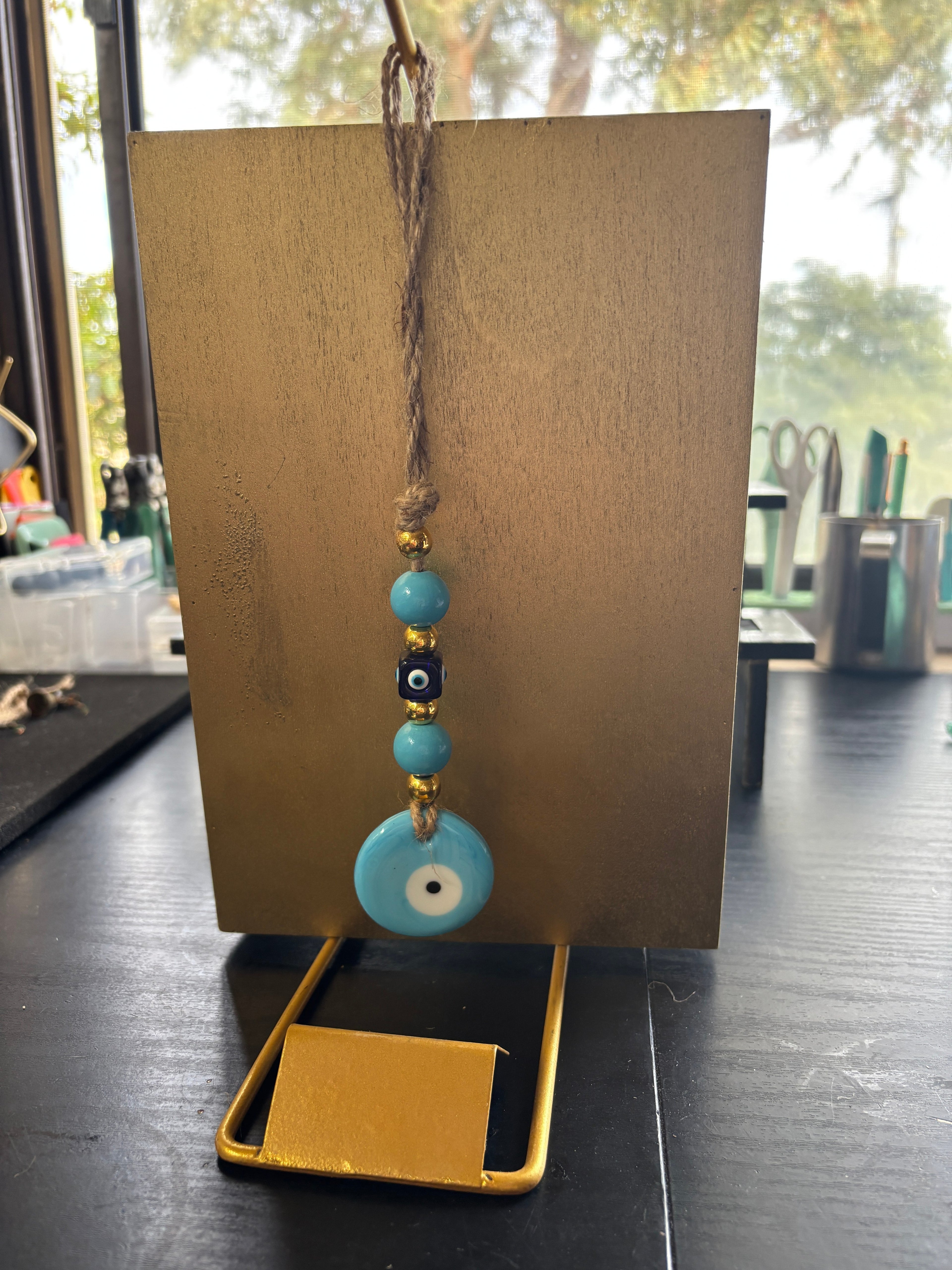 Mati Made evil eye wall hanging with turquoise beads and gold accents suspended on a rustic twine cord.