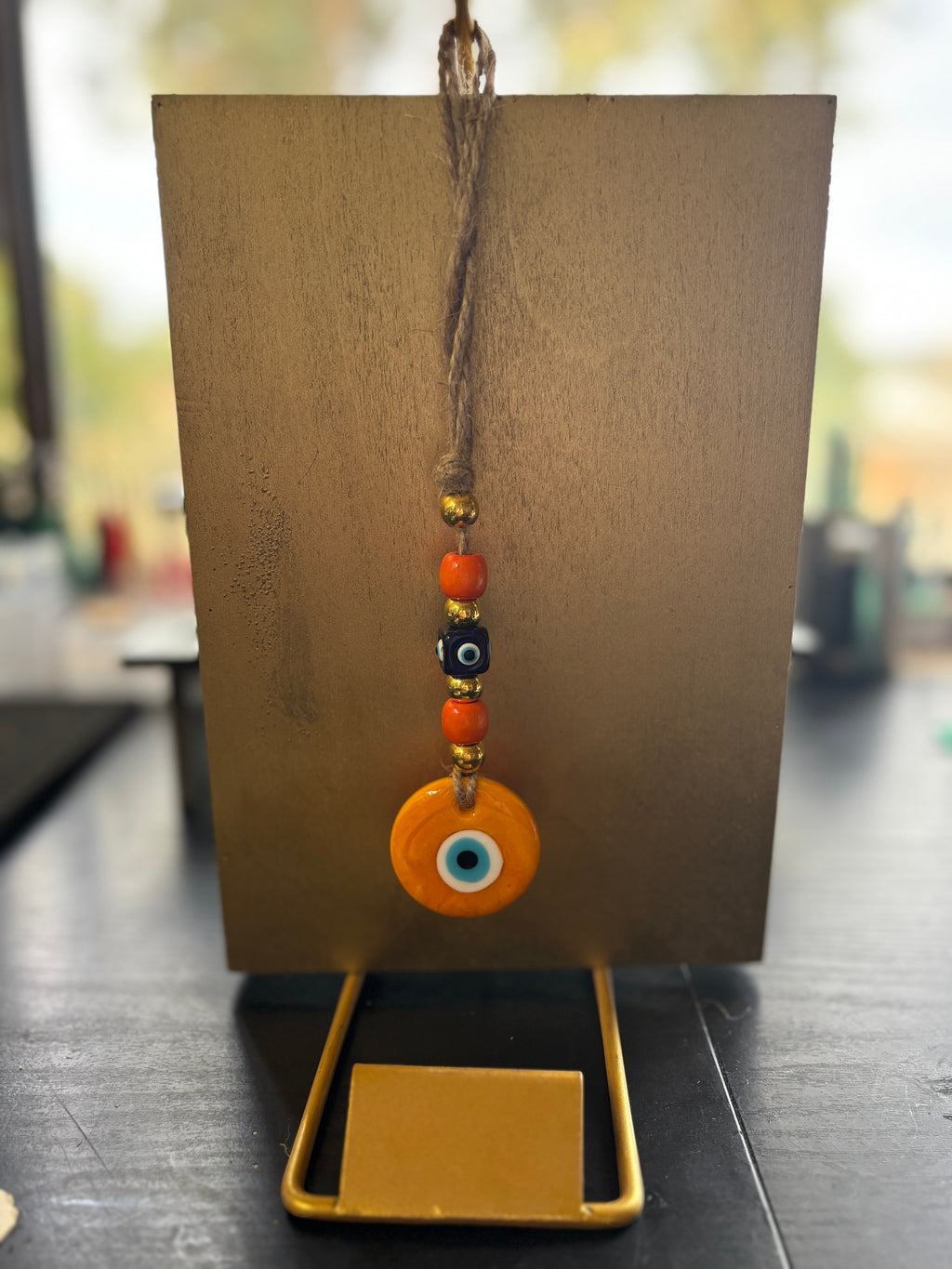Mati Made evil eye wall hanging ornament with orange and black glass beads on a rustic twine string