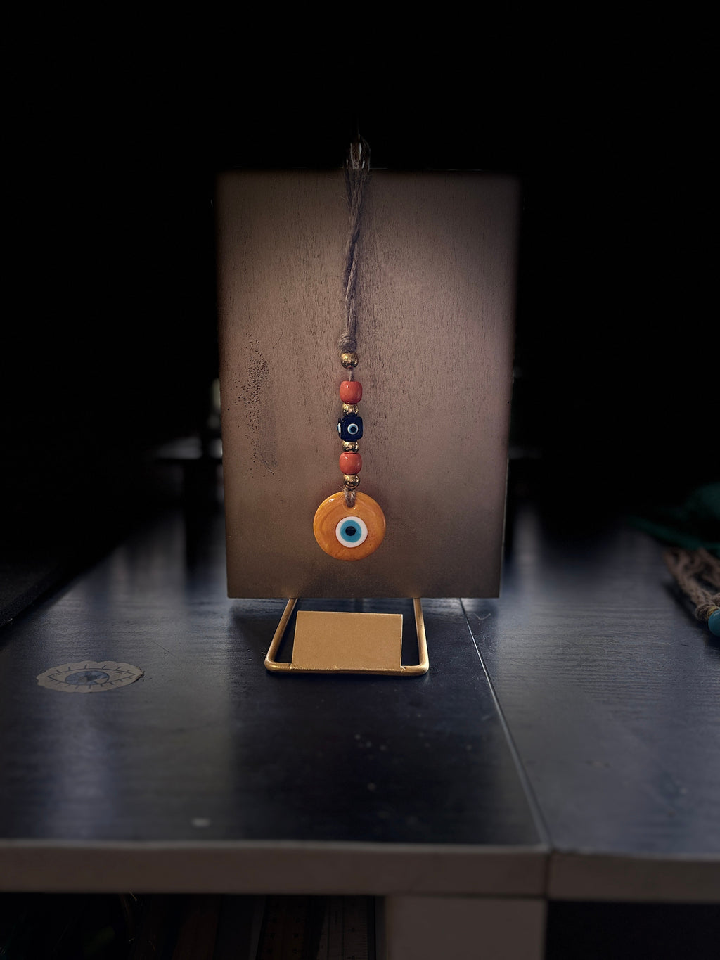 Mati Made evil eye wall hanging ornament with orange and blue beads on a gold display stand