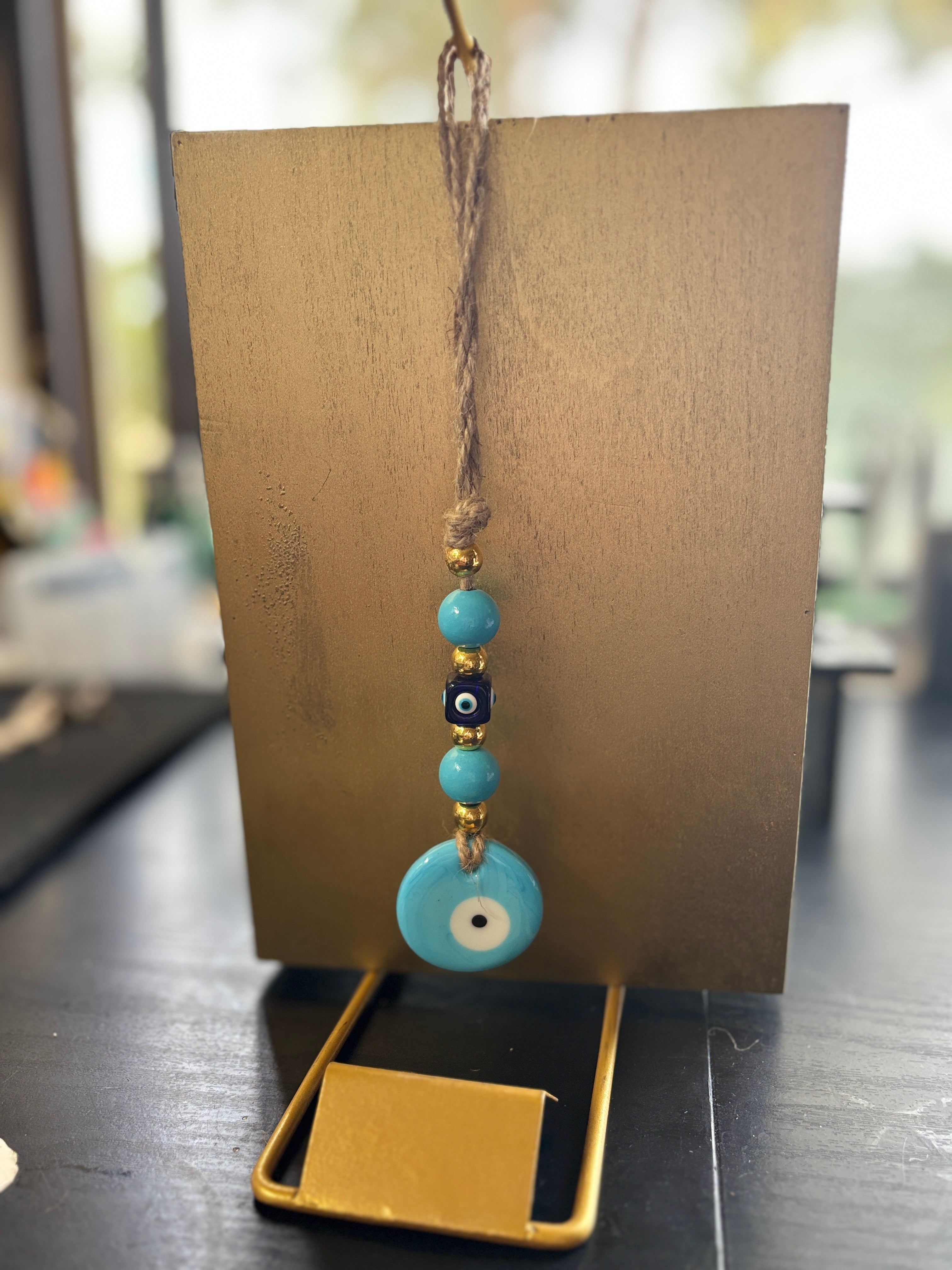 Mati Made evil eye wall hanging ornament with turquoise beads and gold accents on a jute string