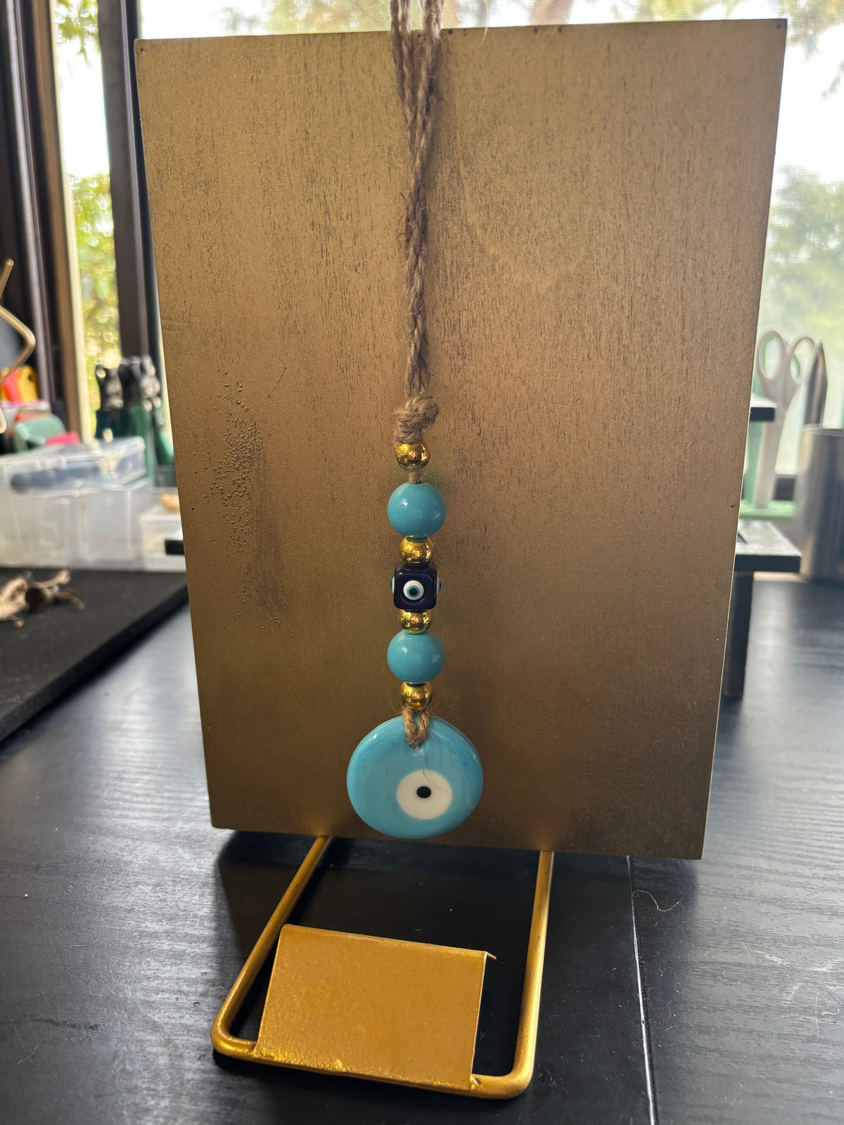 Mati Made evil eye wall hanging ornament with blue glass beads and gold accents on a rustic twine string