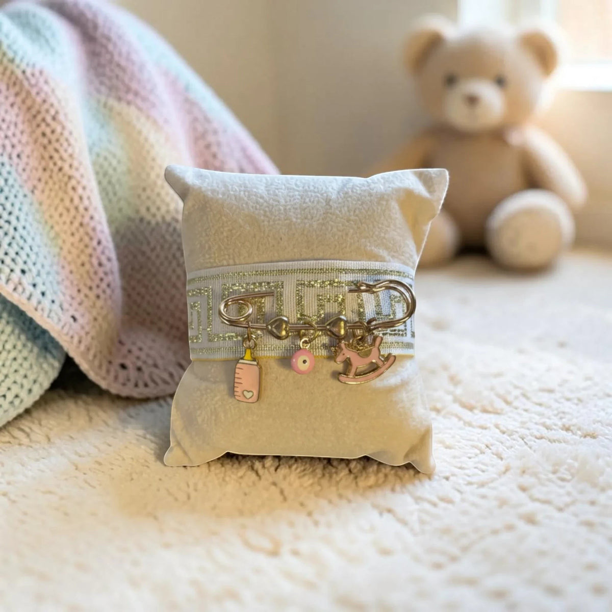 Mati Made Filaxto pillow in soft neutral fabric with a silver-patterned ribbon and charms of a bottle, mati, and horse.