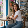 Mati Made curved glass tumbler with green evil eye decal held by a woman sitting at a cafe table with iced coffee.