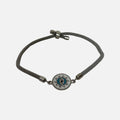 Mati Made grey cord bracelet featuring a circular evil eye charm with white enamel, blue accents, and crystals.
