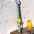 Mati Made handcrafted light blue macrame wall hanging with a yellow evil eye charm and decorative beads.