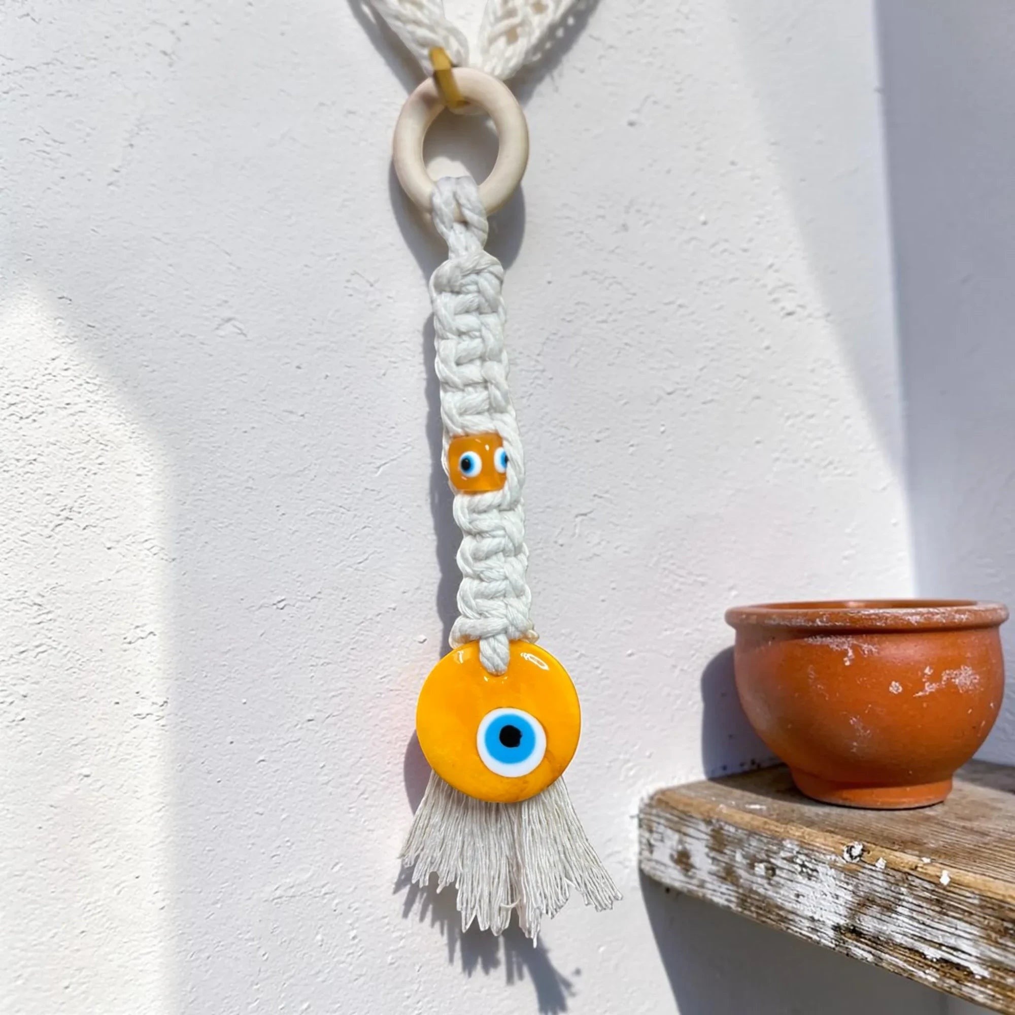 Mati Made handcrafted white cotton macrame wall hanging featuring yellow glass evil eye beads and a wooden ring.