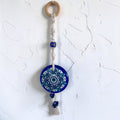 Mati Made mandala evil eye wall charm with blue acrylic disc, macrame cord, wooden ring, and decorative tassel.