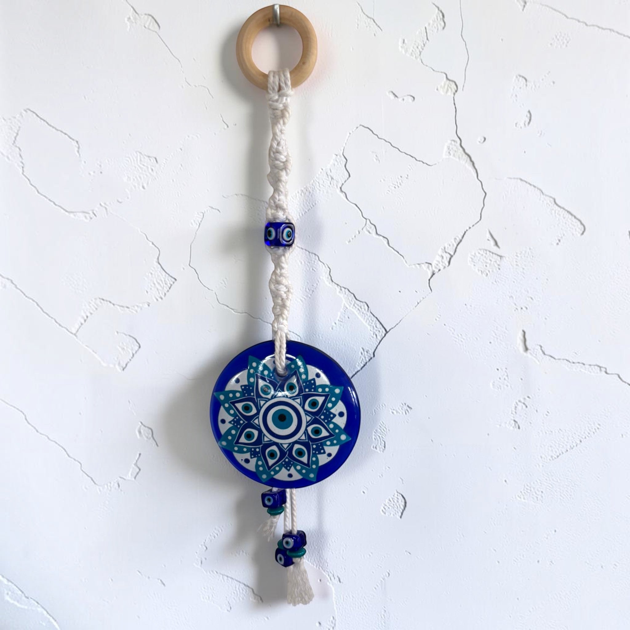 Mati Made mandala evil eye wall charm with blue acrylic disc, macrame cord, wooden ring, and decorative tassel.