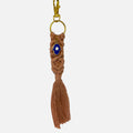 Mati Made peach macrame keychain with a blue Hamsa charm, gold clasp, and tassel detail on a white textured background.