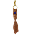 Mati Made peach macrame keychain with a blue Hamsa charm, gold clasp, and tassel detail on a white textured background.