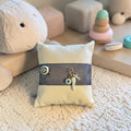 Mati Made protective baby nursery pin with evil eye, cross, and horn charms on a cream velvet cushion with navy ribbon