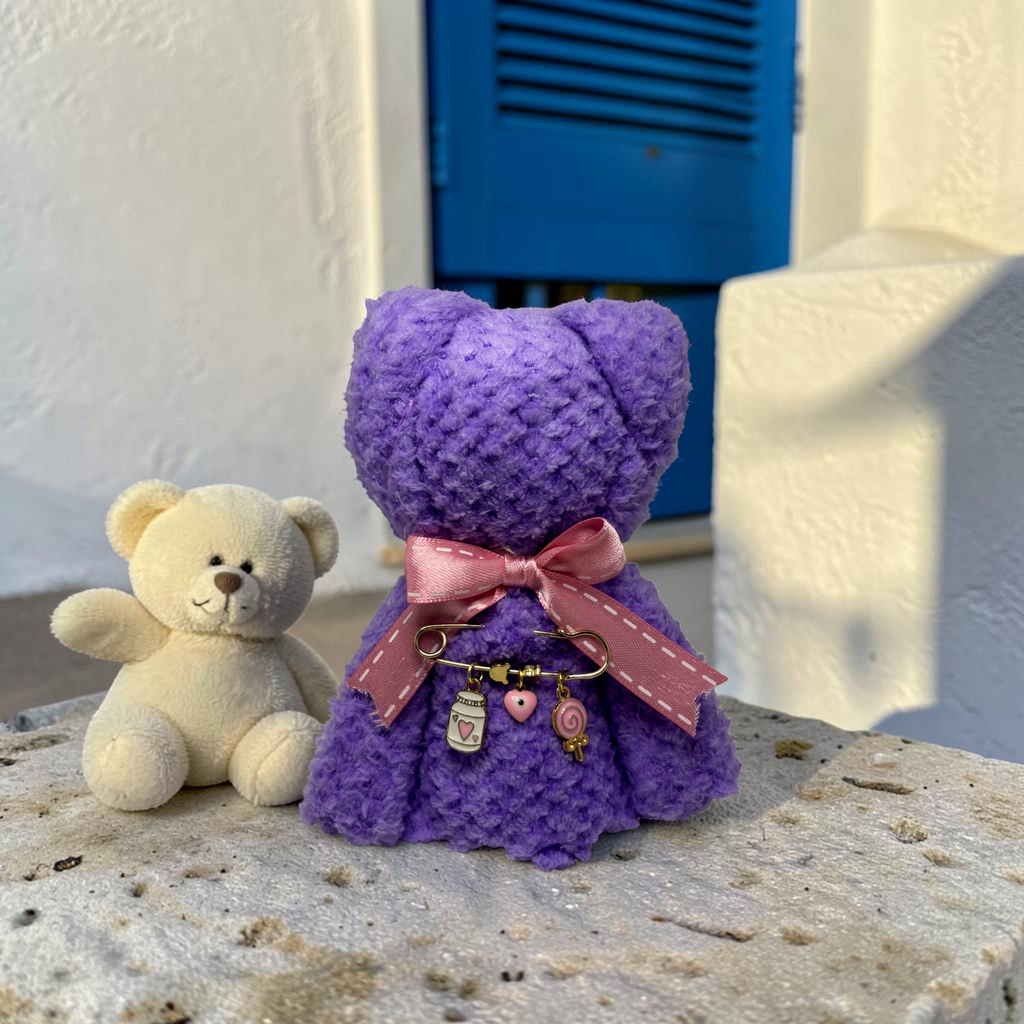 Mati Made purple teddy cloth with pink ribbon and gold filaxto charms next to a small cream teddy bear